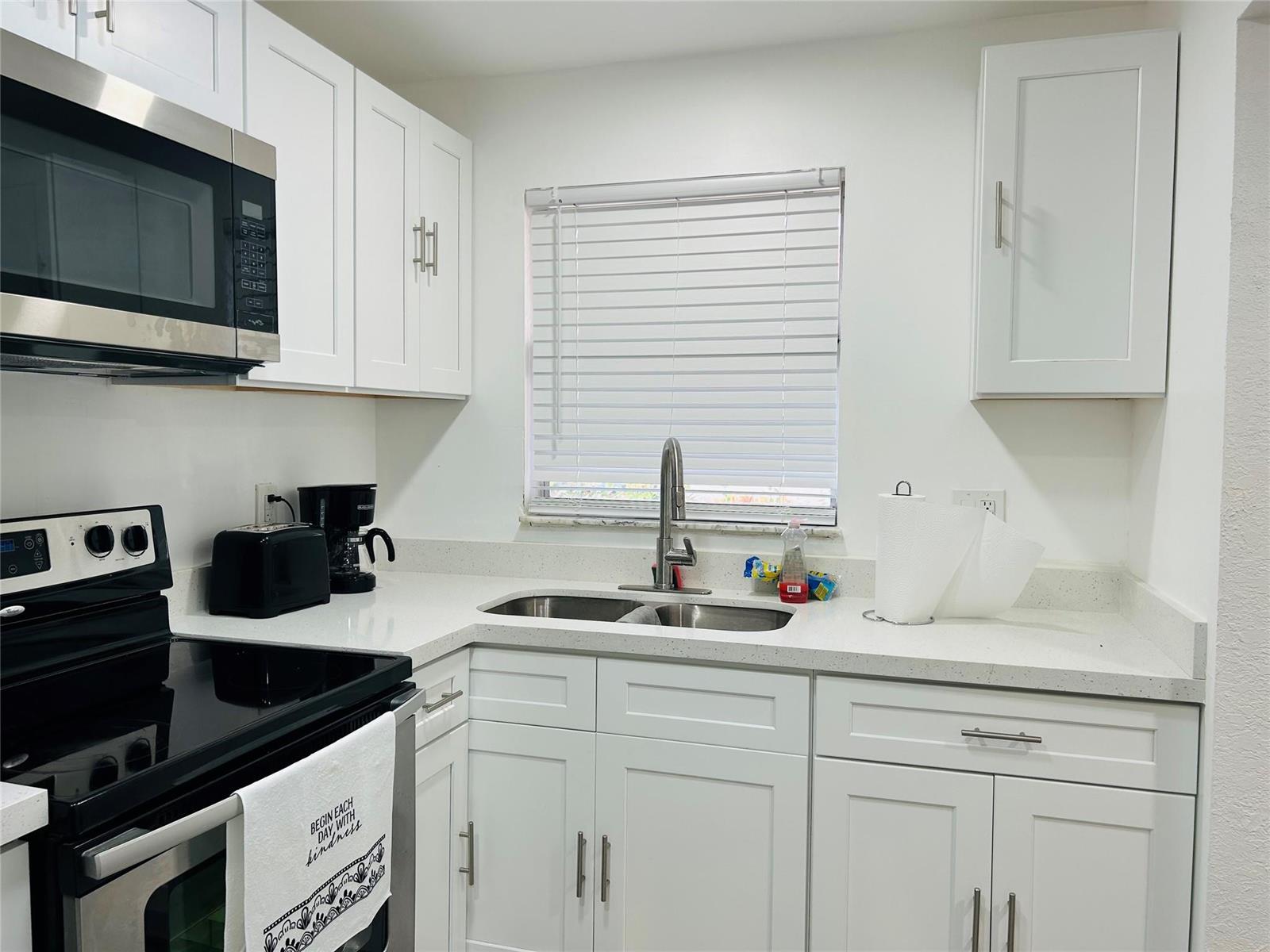 A white kitchen features stainless steel appliances, quartz countertops, and shaker-style cabinets — 2871 E Sunrise Lakes Drive # 101, Sunrise FL 33322, SUNRISE, FL