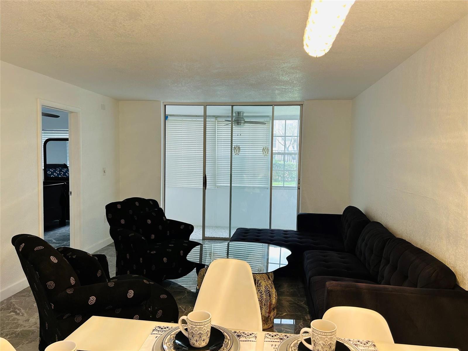 A living room with dark furniture, a glass coffee table, and a sliding glass door — 2871 E Sunrise Lakes Drive # 101, Sunrise FL 33322, SUNRISE, FL