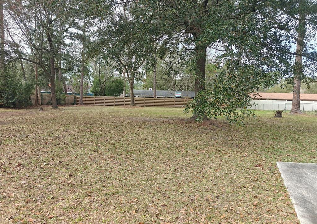 A grassy backyard features mature trees, a wooden fence, and a concrete patio edge — NW 29TH TERRACE, GAINESVILLE, FL