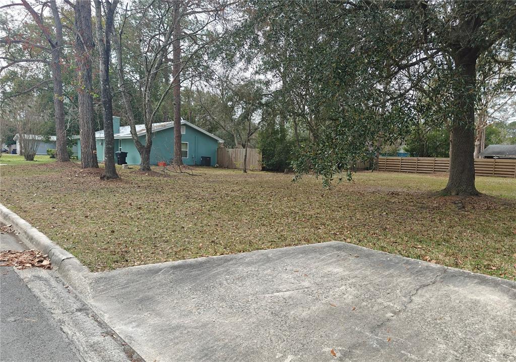 A view of a grassy vacant lot next to a teal house with trees — NW 29TH TERRACE, GAINESVILLE, FL