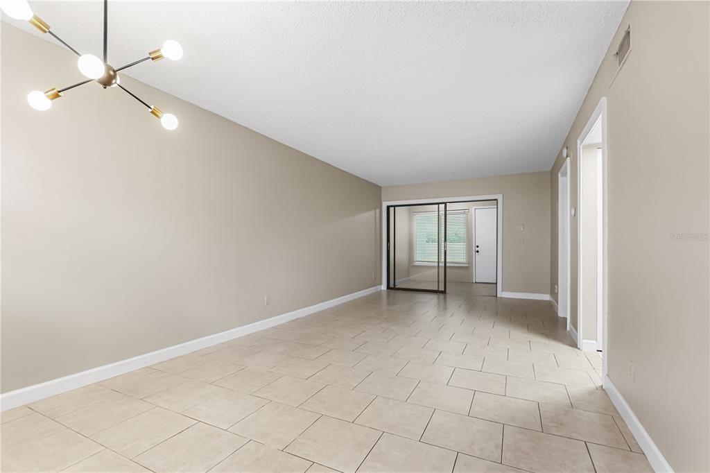 An empty room with beige walls, light tile flooring, and a modern sputnik chandelier — 3036 EASTLAND BOULEVARD UNIT E104, CLEARWATER, FL