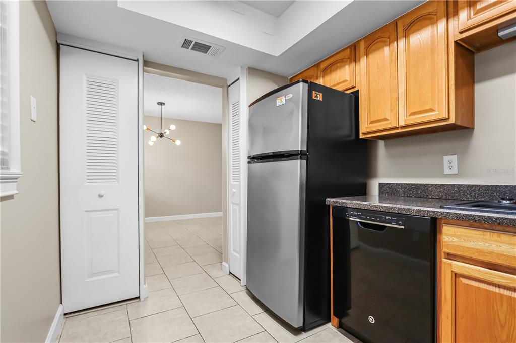 A kitchen features a stainless steel refrigerator, black dishwasher, wood cabinets, and tile flooring — 3036 EASTLAND BOULEVARD UNIT E104, CLEARWATER, FL