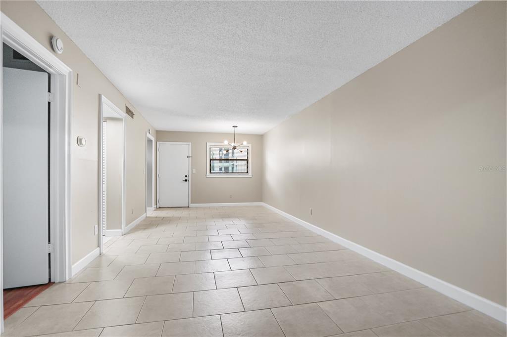 An empty room with beige walls, light-colored tile flooring, and a central light fixture — 3036 EASTLAND BOULEVARD UNIT E104, CLEARWATER, FL