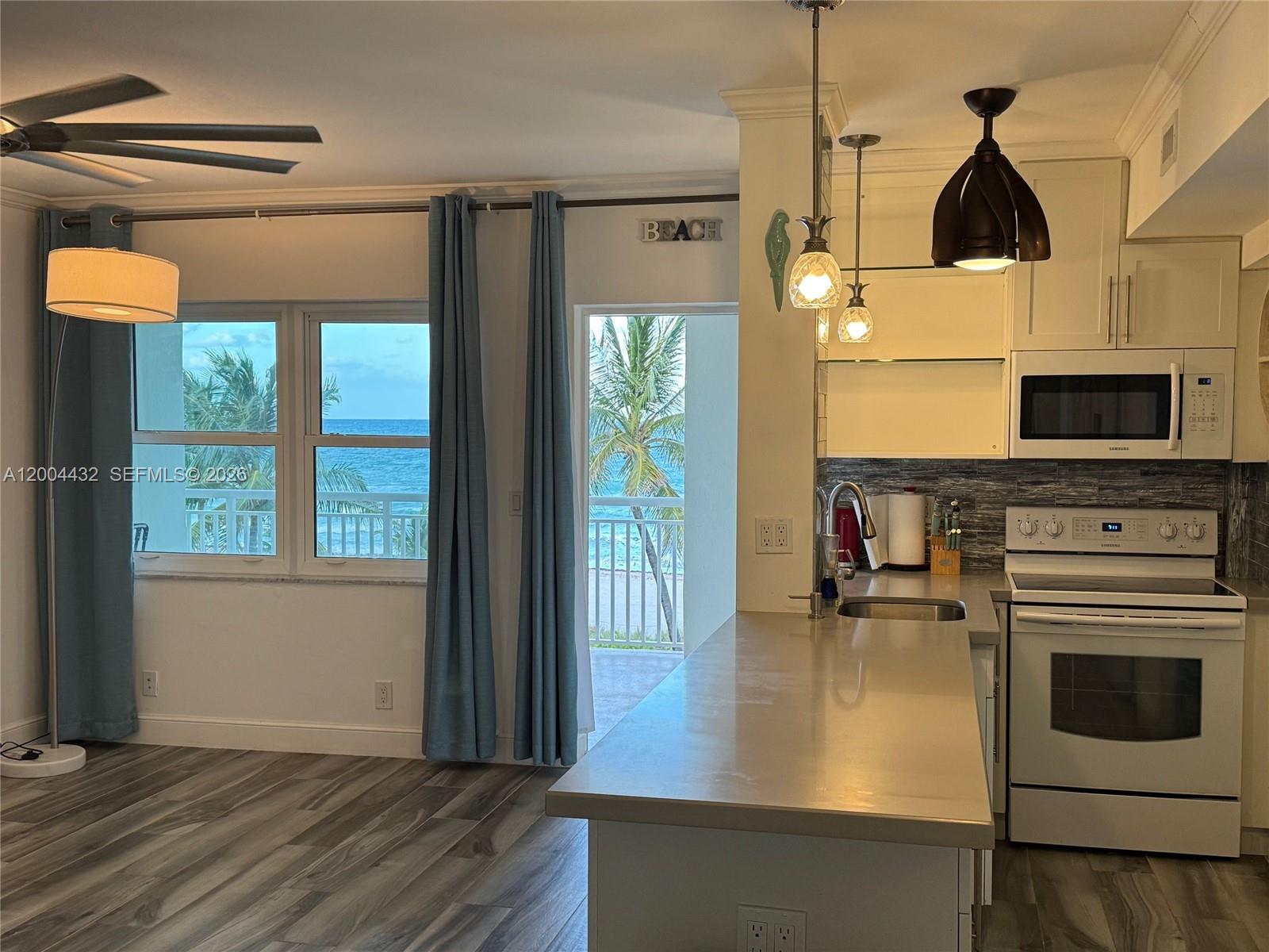 A kitchen with white cabinets and appliances overlooks a balcony with ocean views — 901 S Surf Rd # 407, Hollywood FL 33019, HOLLYWOOD, FL