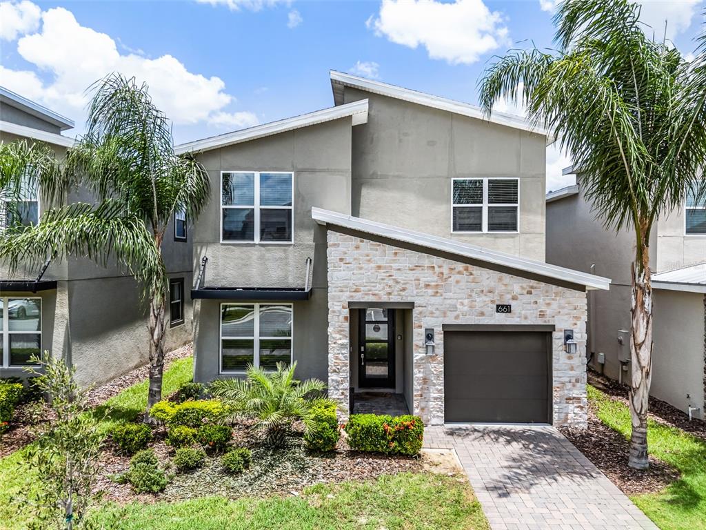A two-story house features a stone facade, a single-car garage, and palm trees in front — 661 DROP SHOT DRIVE, DAVENPORT, FL
