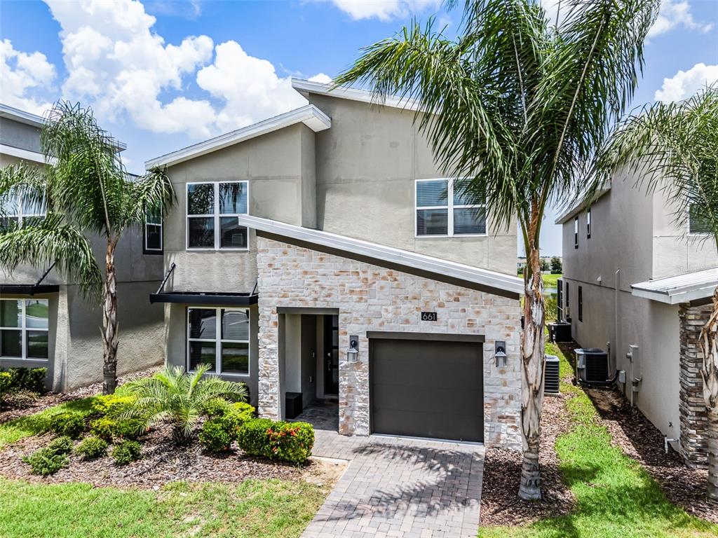 A two-story house features a stone-veneer facade, a single-car garage, and palm trees in front — 661 DROP SHOT DRIVE, DAVENPORT, FL