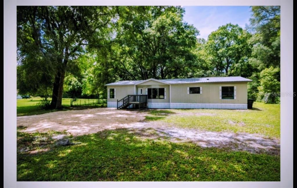 A single-story manufactured home with tan siding sits on a grassy lot with large trees — 14902 NE 142ND STREET, WALDO, FL