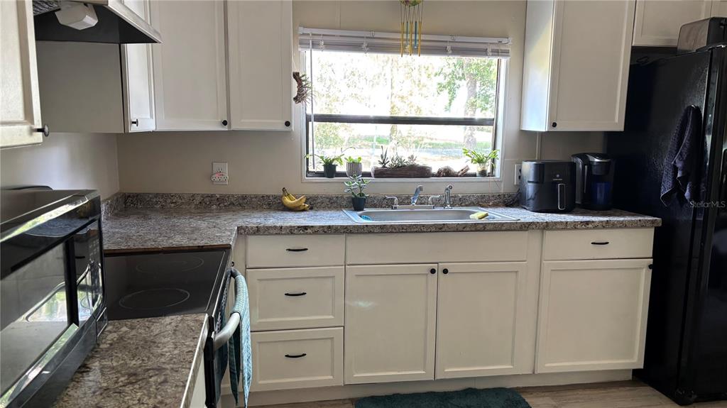 A kitchen features white cabinets, a speckled countertop, a stainless steel sink, and black appliances — 14902 NE 142ND STREET, WALDO, FL