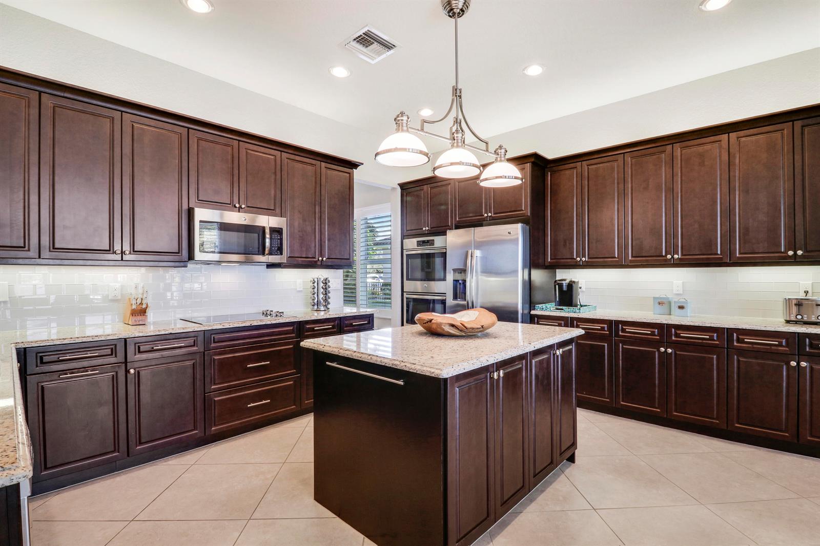 A kitchen features dark wood cabinets, granite countertops, stainless steel appliances, and a central island — 7754 Maywood Crest Drive, West Palm Beach FL 33412, WEST PALM BEACH, FL