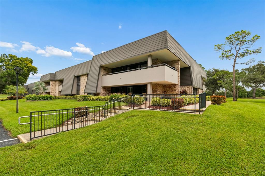 A two-story building with brick and gray siding features a balcony and black metal fencing — 36750 US HIGHWAY 19 N UNIT 11206, PALM HARBOR, FL