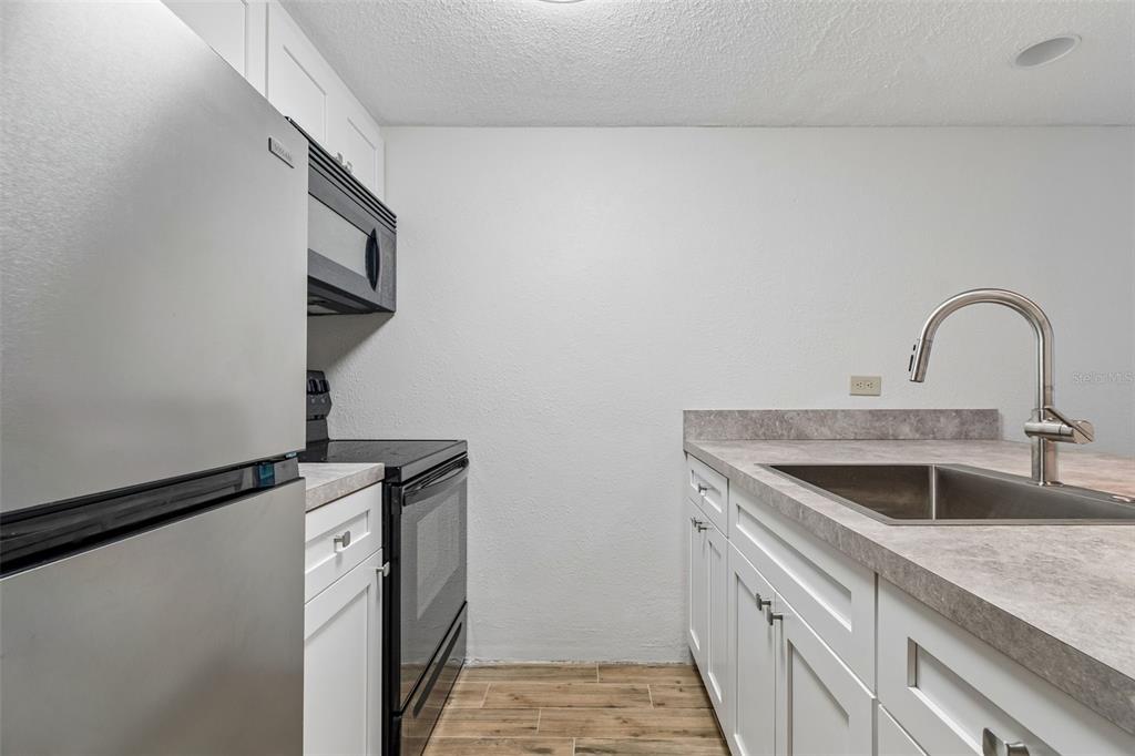 A kitchen features white cabinets, stainless steel appliances, a gray countertop, and wood-look flooring — 36750 US HIGHWAY 19 N UNIT 11206, PALM HARBOR, FL