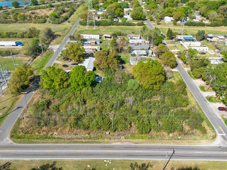 An aerial view shows a vacant, overgrown lot bordered by roads and nearby residential properties — 7623 S 51ST AVENUE, TAMPA, FL