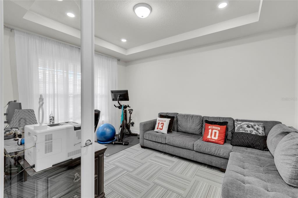 A home office features a gray sectional sofa, a stationary bike, and a desk with a printer — 7537 WANDERING WAY, ORLANDO, FL