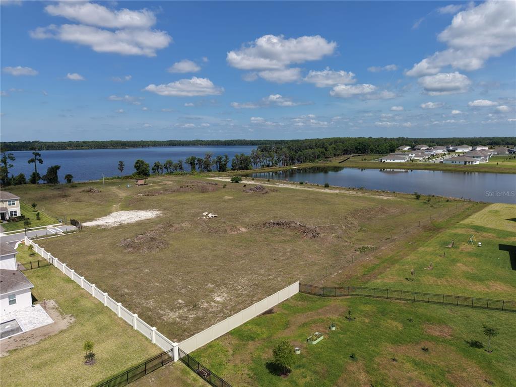 An aerial view shows a large, undeveloped grassy lot bordered by fences and a lake — LAKE PICKETT RD, ORLANDO, FL