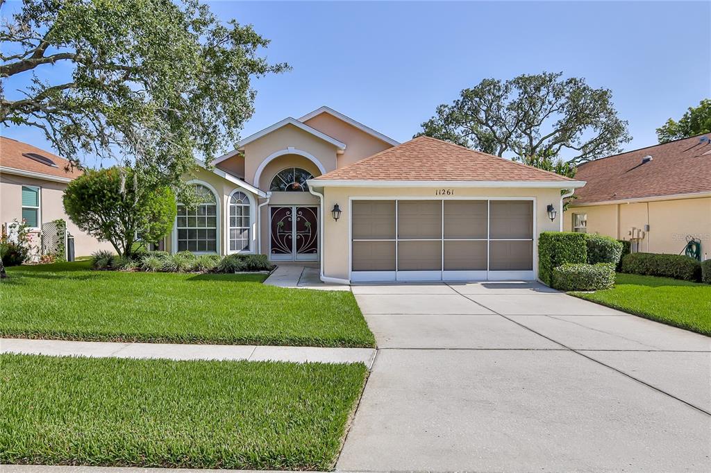 A single-story house with a tan stucco exterior, a screened garage, and a front lawn — 11261 MCRACKEN DRIVE, SPRING HILL, FL