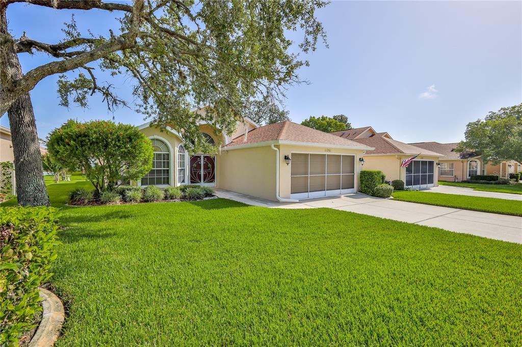 A single-story house with a beige stucco exterior, a two-car garage, and a green lawn — 11261 MCRACKEN DRIVE, SPRING HILL, FL