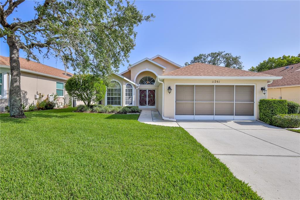 A single-story house with a tan exterior, a two-car garage, and a front lawn — 11261 MCRACKEN DRIVE, SPRING HILL, FL