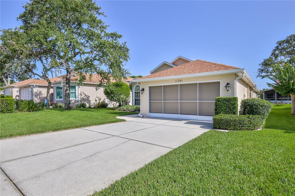A tan single-story house features a screened-in garage door and a concrete driveway — 11261 MCRACKEN DRIVE, SPRING HILL, FL