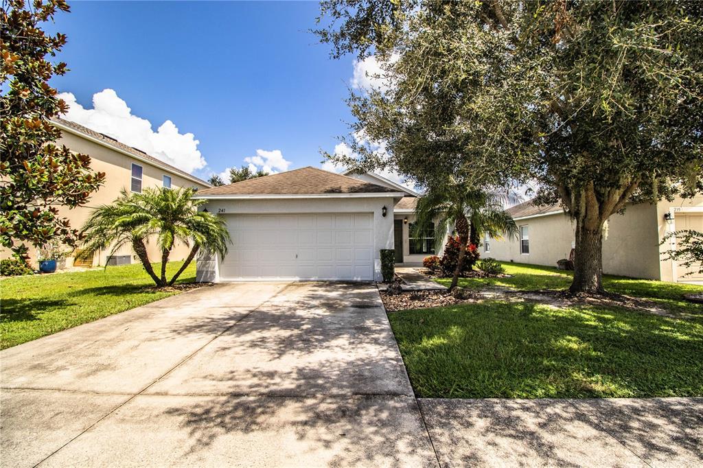 A single-story house with a white garage door, a concrete driveway, and surrounding trees — 241 GROVE BRANCH ROAD, WINTER HAVEN, FL