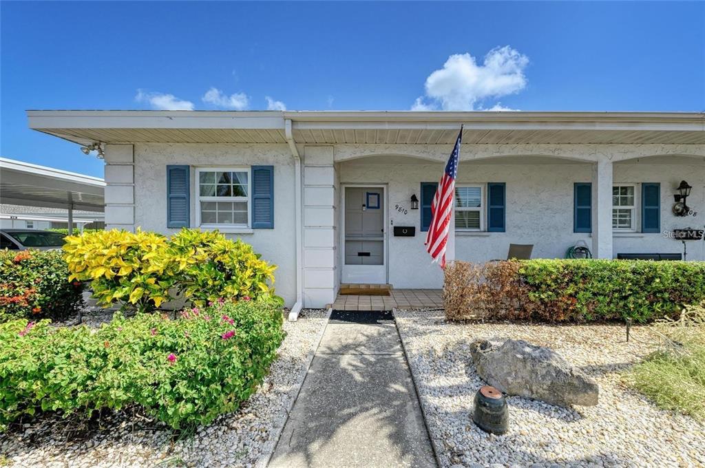A single-story house exterior features a front porch, an American flag, and landscaped bushes — 9810 DORADO AVENUE UNIT 9810, BRADENTON, FL