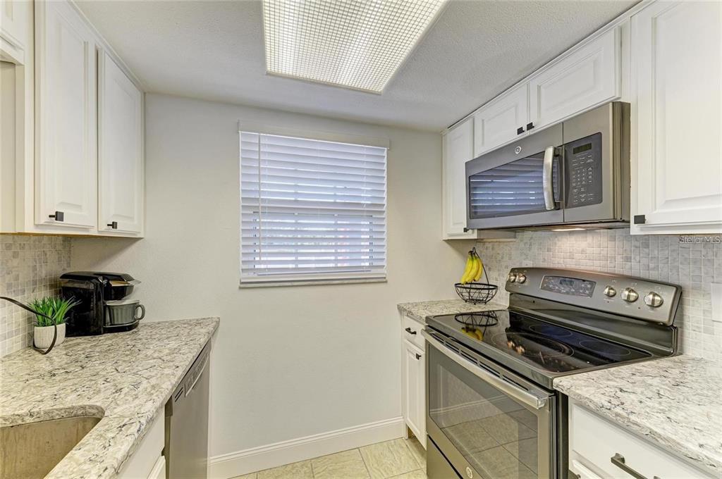 A kitchen features white cabinets, granite countertops, a stainless steel microwave, and a glass-top stove — 9810 DORADO AVENUE UNIT 9810, BRADENTON, FL