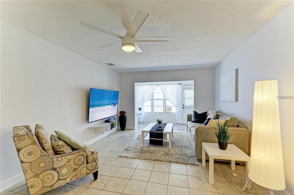 A living room features tile flooring, a ceiling fan, a wall-mounted television, and a sofa — 9810 DORADO AVENUE UNIT 9810, BRADENTON, FL