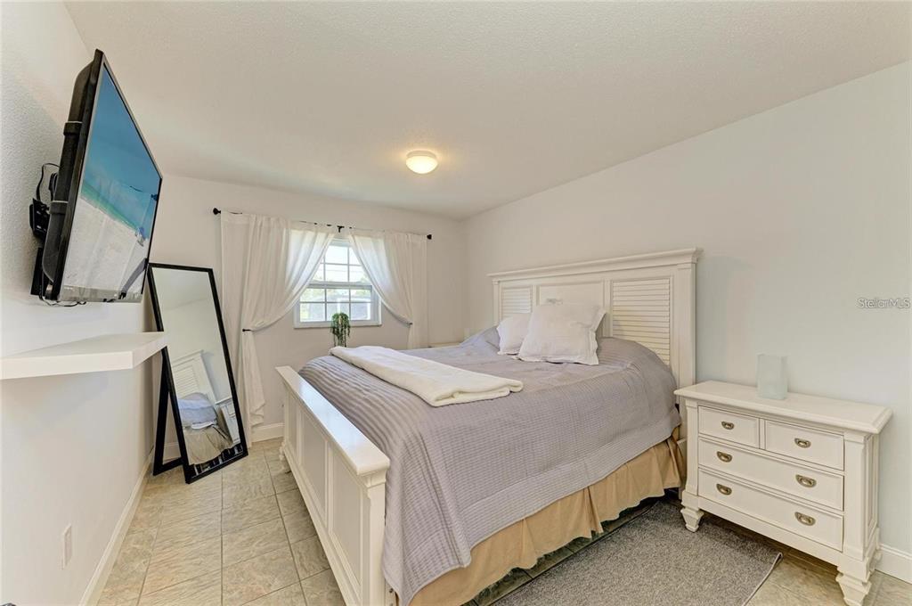 A bedroom features a white bed frame, a matching nightstand, a floor mirror, and a television — 9810 DORADO AVENUE UNIT 9810, BRADENTON, FL