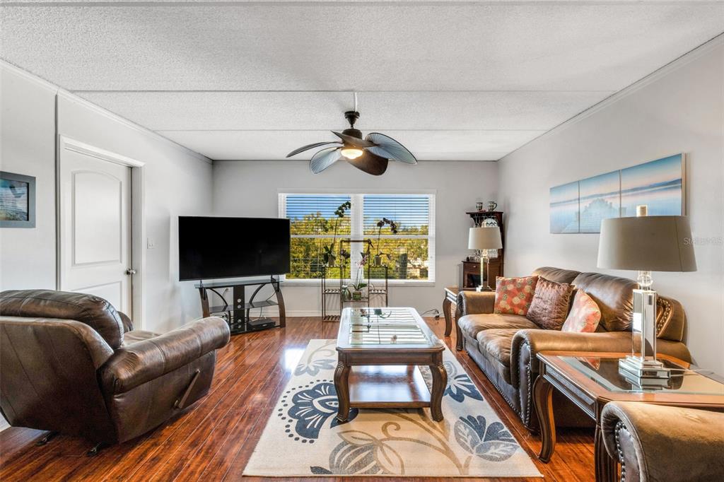 A living room and dining area with hardwood floors, brown leather furniture, and a ceiling fan — 12760 INDIAN ROCKS ROAD UNIT 119, LARGO, FL