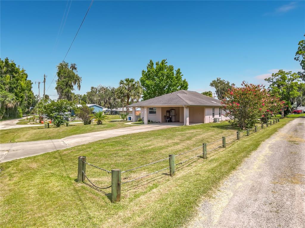 A single-story house with a carport sits on a grassy lot with a wire fence — 30620 NE 95TH PLACE, FORT MC COY, FL