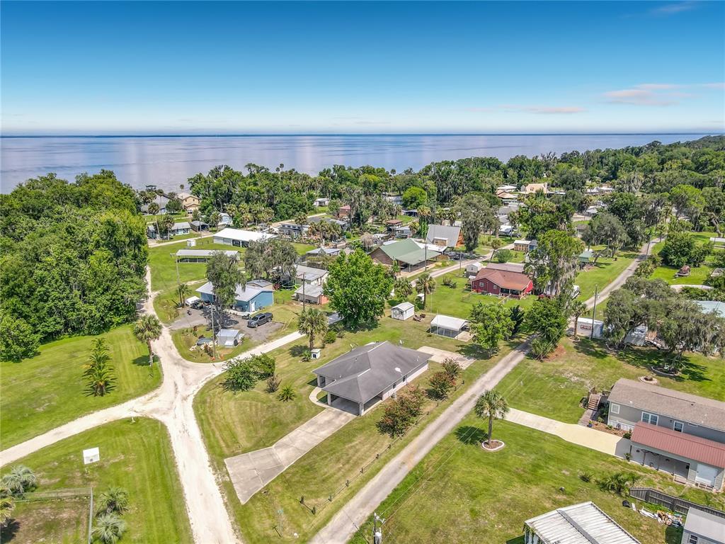 An aerial view shows a residential neighborhood with houses, green lawns, and trees near water — 30620 NE 95TH PLACE, FORT MC COY, FL