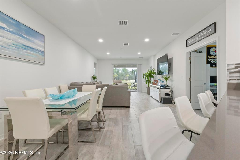 An open-concept living and dining area features light wood-look tile flooring and white walls — 1184 SAND TRAP COURT, DAYTONA BEACH, FL