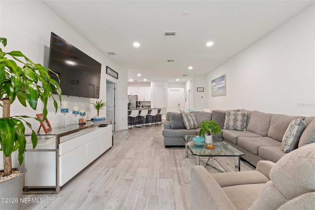 A living room features light wood-look flooring, a gray sectional sofa, and a wall-mounted television — 1184 SAND TRAP COURT, DAYTONA BEACH, FL