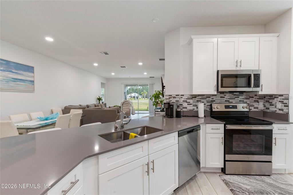 A kitchen with white cabinets and gray countertops overlooks an open-concept dining and living area — 1184 SAND TRAP COURT, DAYTONA BEACH, FL