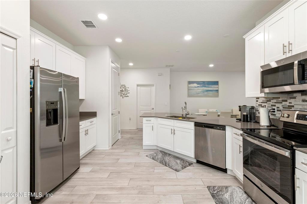 A modern kitchen features white cabinets, stainless steel appliances, and light wood-look flooring — 1184 SAND TRAP COURT, DAYTONA BEACH, FL