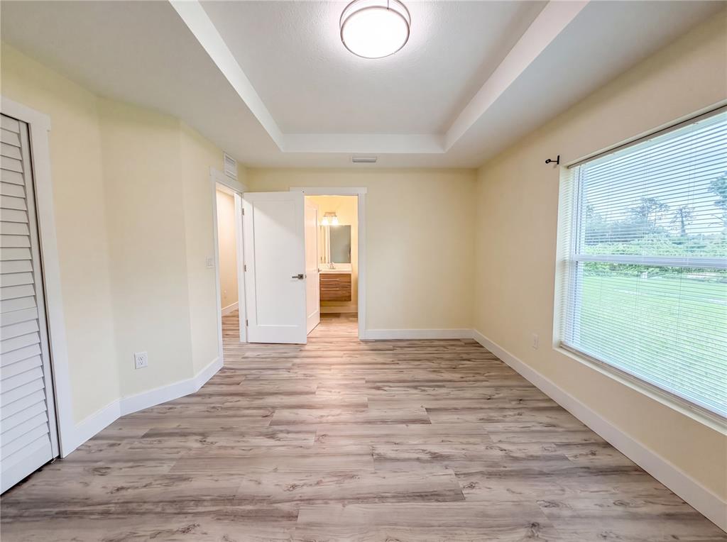 A bedroom with light-colored walls, wood-look flooring, a tray ceiling, and an attached bathroom — 1914 LANDAU AVENUE, NORTH PORT, FL