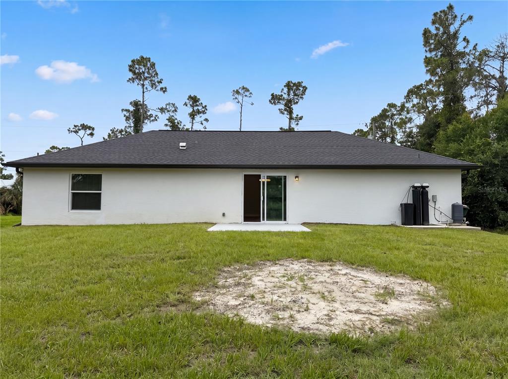 The rear exterior of a white single-story house features a sliding glass door and lawn — 1914 LANDAU AVENUE, NORTH PORT, FL