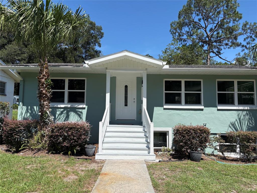 A light green single-story house features a white front door, stairs, and a palm tree — 2094 PENN DRIVE, DELAND, FL