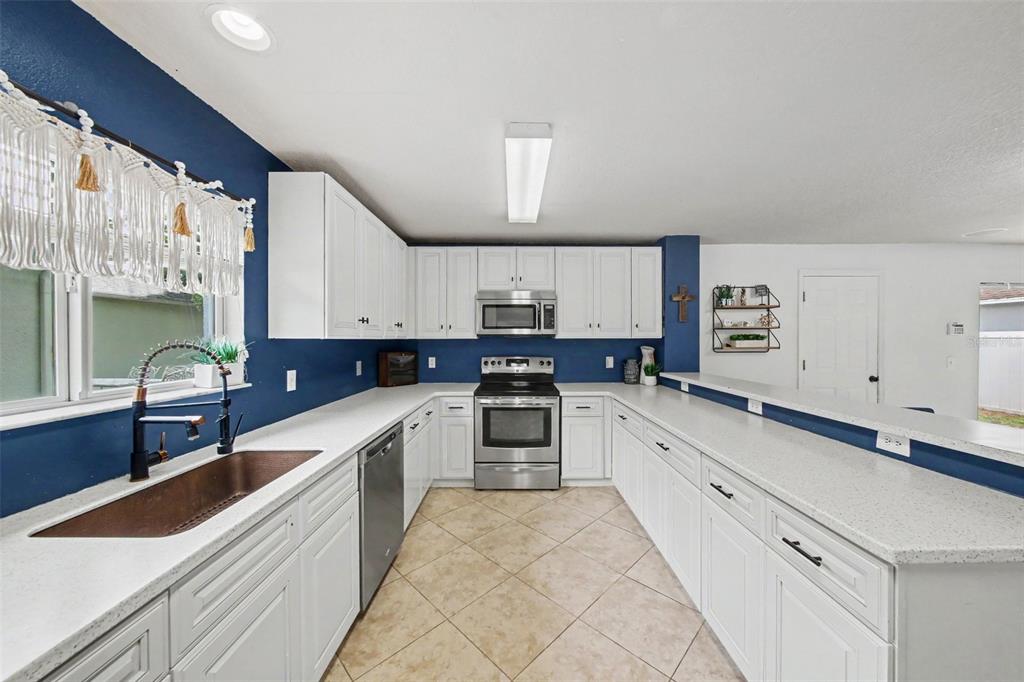 A kitchen features white cabinets, a dark blue backsplash, stainless steel appliances, and quartz countertops — 13626 PHOENIX, ORLANDO, FL