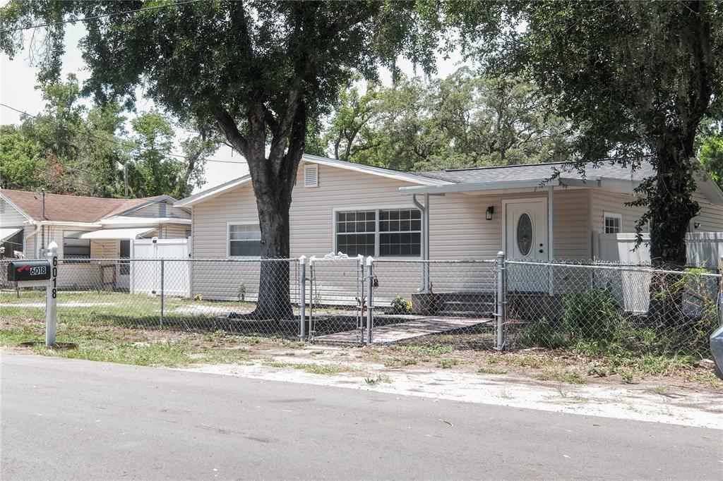 A single-story house with light-colored siding is enclosed by a chain-link fence — 6018 N 49TH STREET, TAMPA, FL