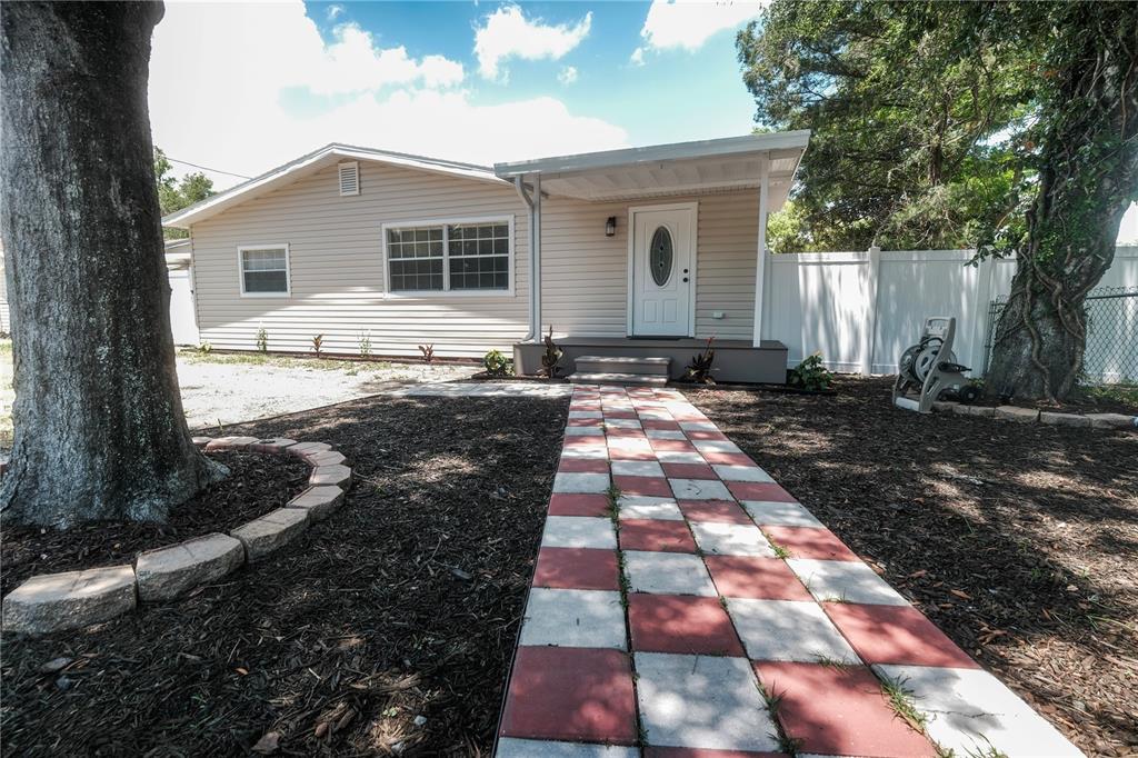 A single-story house with beige siding, a checkered walkway, and large trees in the yard — 6018 N 49TH STREET, TAMPA, FL