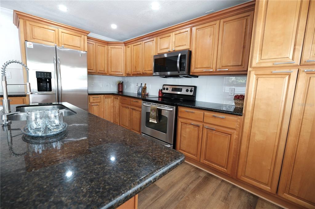 A kitchen features wood cabinets, dark granite countertops, stainless steel appliances, and wood-look flooring — 6018 N 49TH STREET, TAMPA, FL