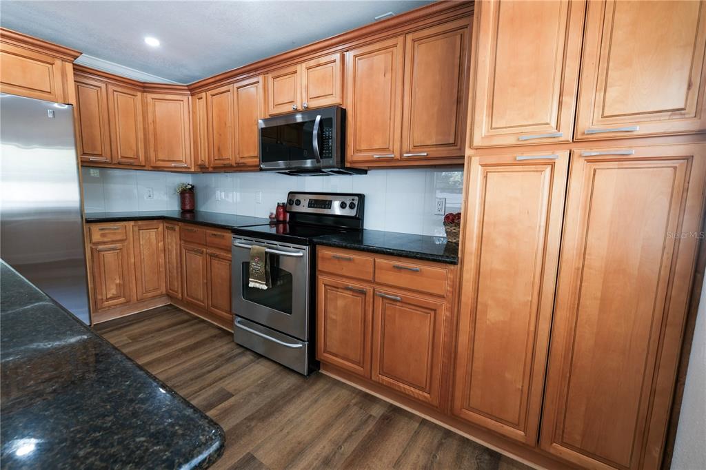 A kitchen features wood cabinets, stainless steel appliances, and dark granite countertops — 6018 N 49TH STREET, TAMPA, FL