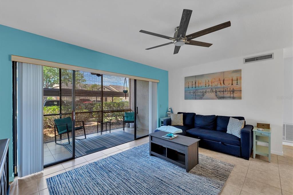 A living room features a blue accent wall, a navy sofa, and sliding glass patio doors — 5669 ASHTON LAKE DRIVE UNIT 1, SARASOTA, FL