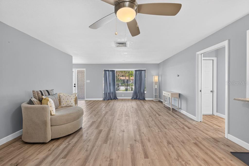 A living room with light gray walls, wood-look flooring, a ceiling fan, and a curved sofa — 2159 GREENBRIAR BOULEVARD, CLEARWATER, FL