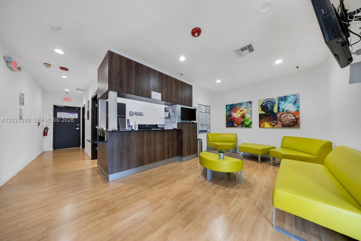 A reception area features a dark wood desk, lime green seating, and light wood flooring — 99 W 49th St, Hialeah FL 33012, HIALEAH, FL