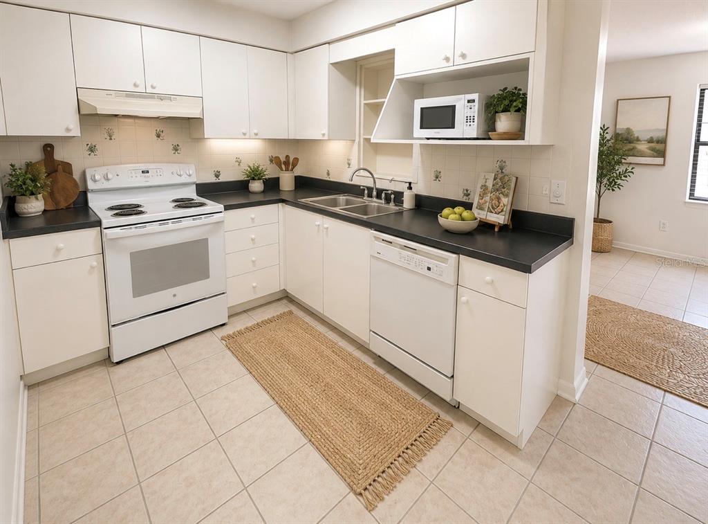 A kitchen features white cabinets, black countertops, white appliances, and light-colored tile flooring — 7310 FILBERT LANE, TAMPA, FL