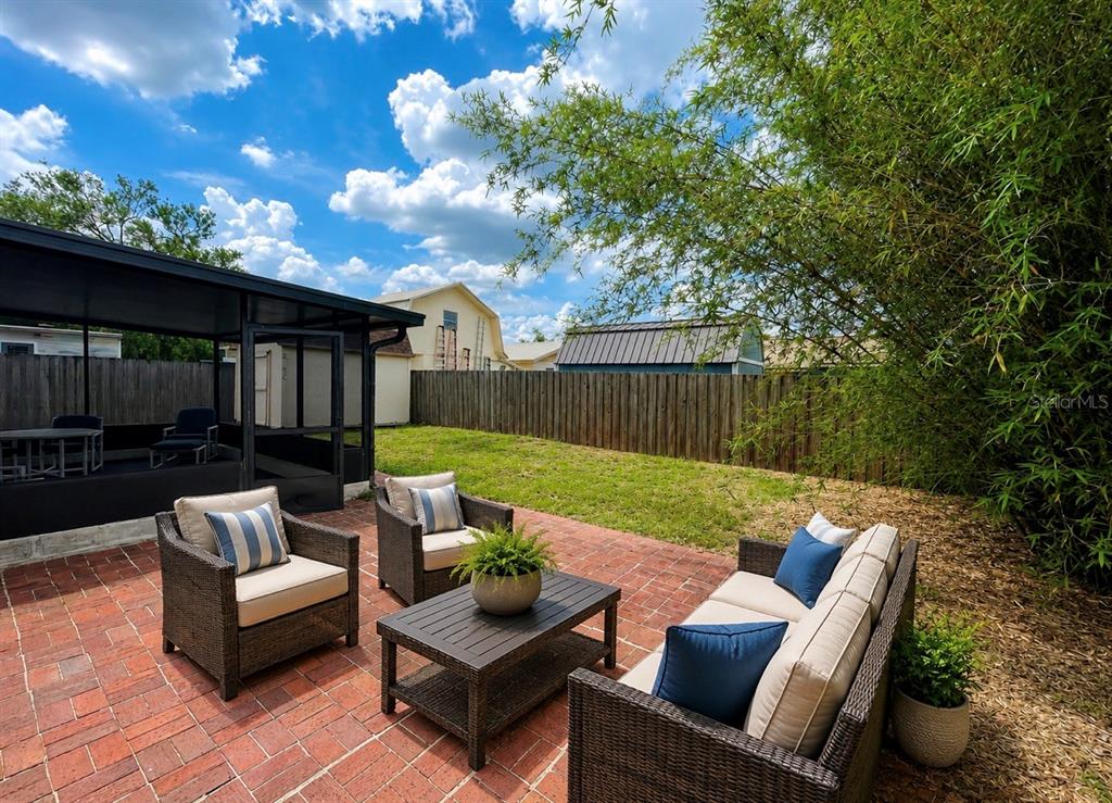 A brick patio features outdoor wicker furniture and a screened-in porch in a backyard — 7310 FILBERT LANE, TAMPA, FL