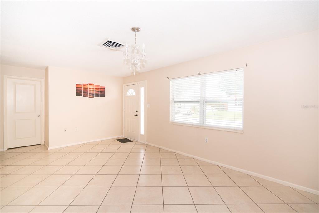 A bright, tiled entryway features a chandelier, a front door, and a multi-panel wall art — 8033 MANVEL DRIVE, PORT RICHEY, FL
