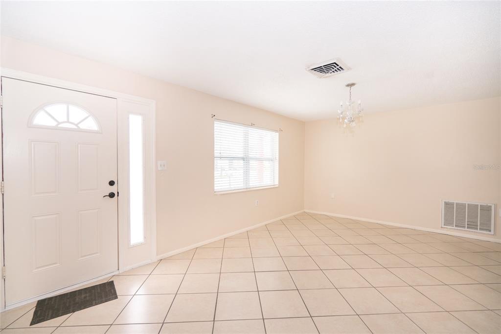 An empty room with beige tile flooring, a white front door, and a chandelier — 8033 MANVEL DRIVE, PORT RICHEY, FL