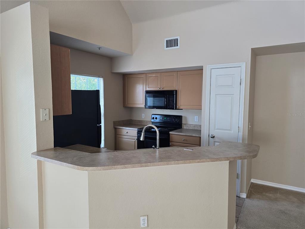 A kitchen with light wood cabinets, black appliances, and a breakfast bar counter — 5601 ROSEHILL ROAD UNIT 203, SARASOTA, FL
